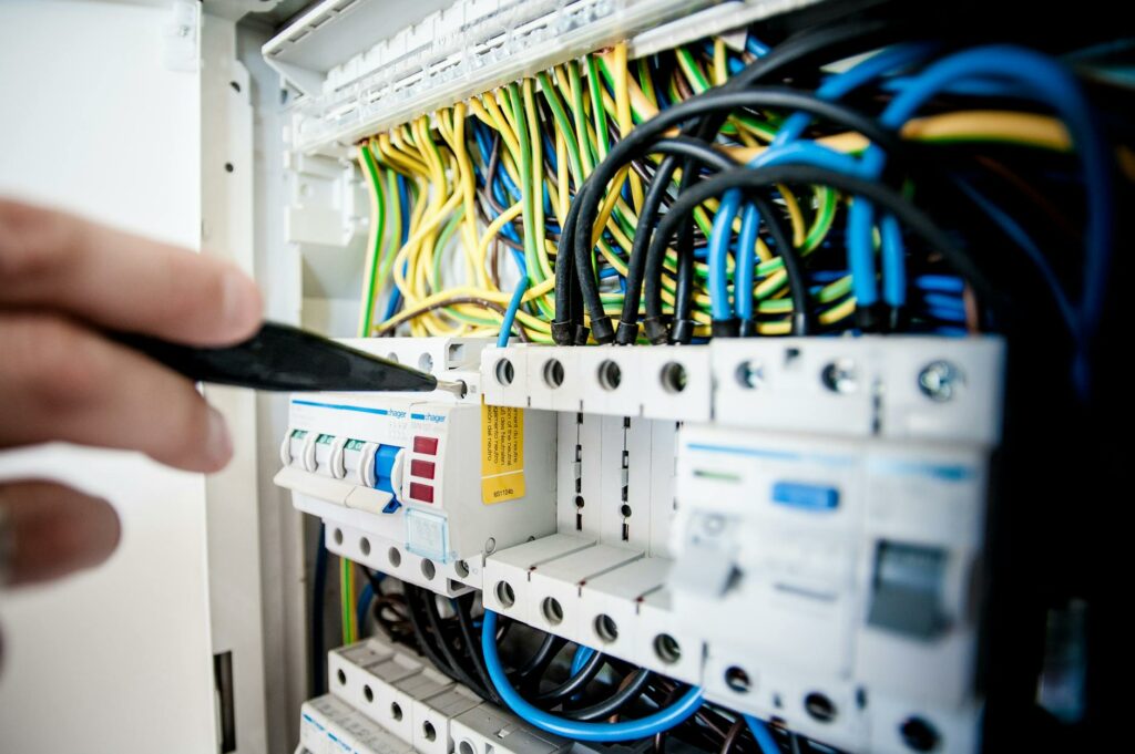 pexels-photo-257736-257736-2 Hand of electrician working on a circuit breaker panel with colorful wires, ensuring safe electrical connections.